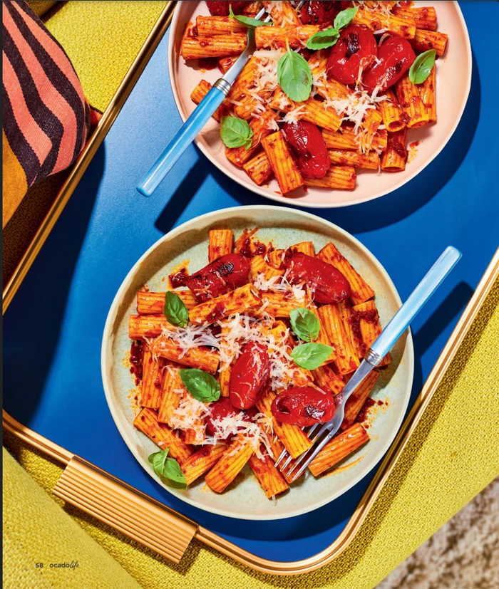Two plates of rigatoni pasta with roasted tomatoes and basil styled on a blue and yellow tray in Sydney by prop stylist Lauren Miller.