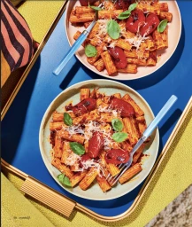 Two plates of rigatoni pasta with roasted tomatoes and basil styled on a blue and yellow tray in Sydney by prop stylist Lauren Miller.
