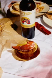 A wine bottle of Other world wines and a piece of lobster on a small amber dish set on a white tablecloth.