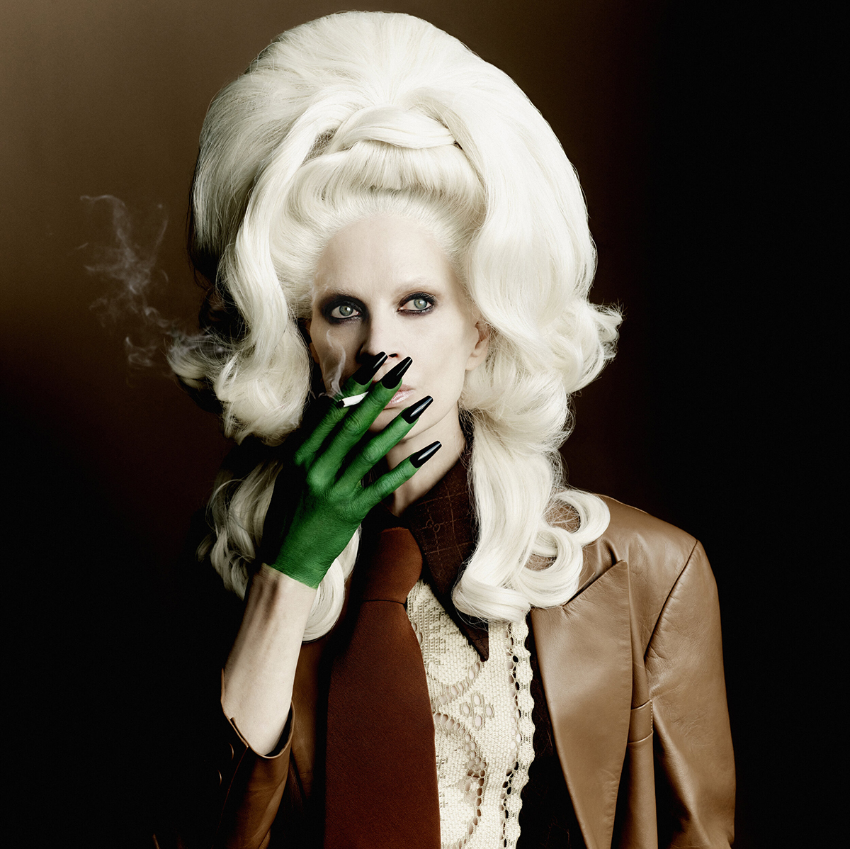 Person in a brown jacket with green gloved hand smoking cigarette against a black background, featuring a large blonde wig.