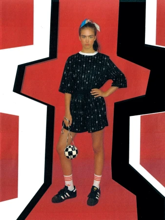 Young woman in patterned shirt and shorts holding soccer ball purse, posing in a geometric, vibrant red and black design.