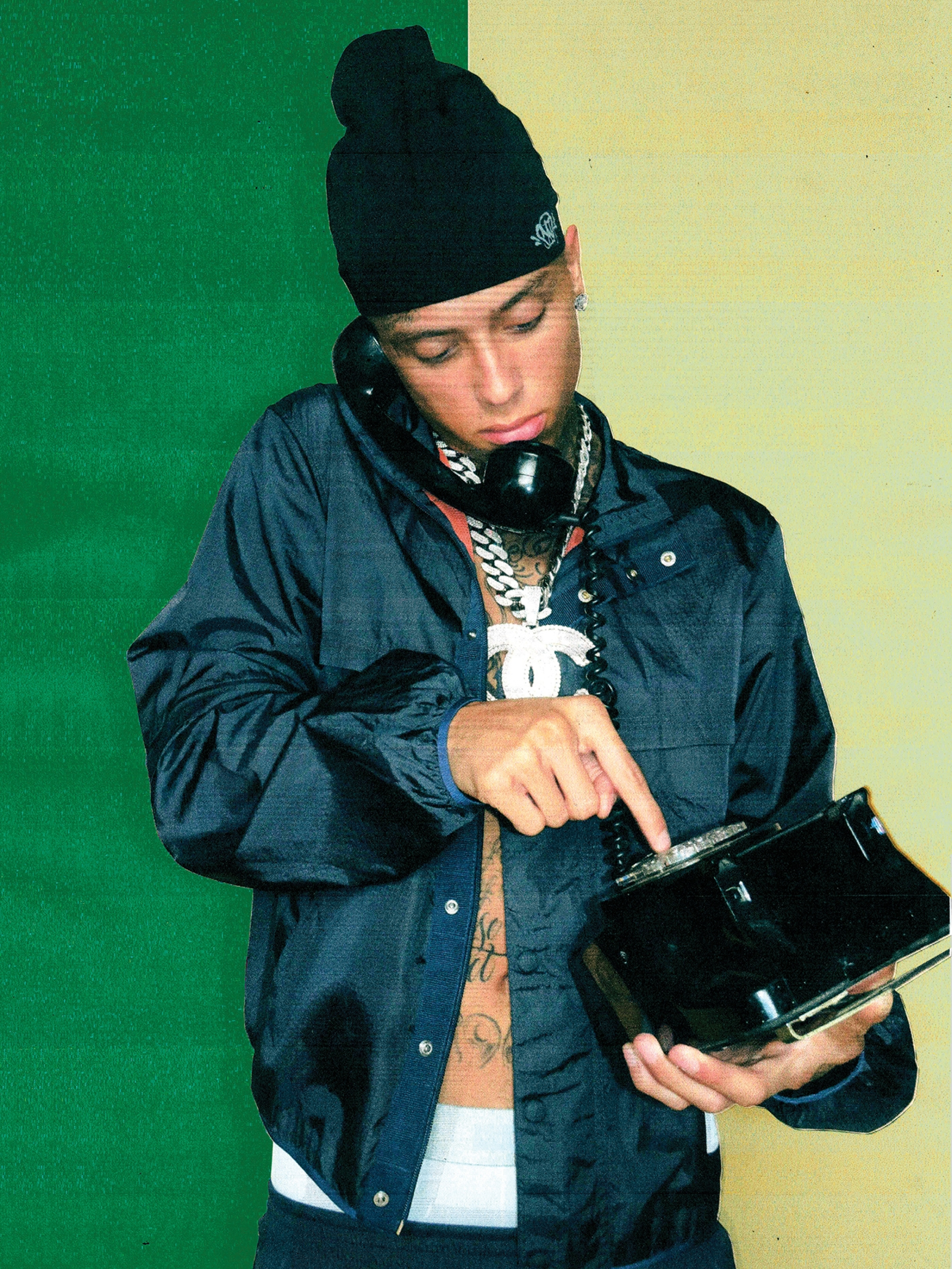 Man wearing a black beanie and jacket, on a retro telephone, against a green and yellow background, gold chain, and tattoos.