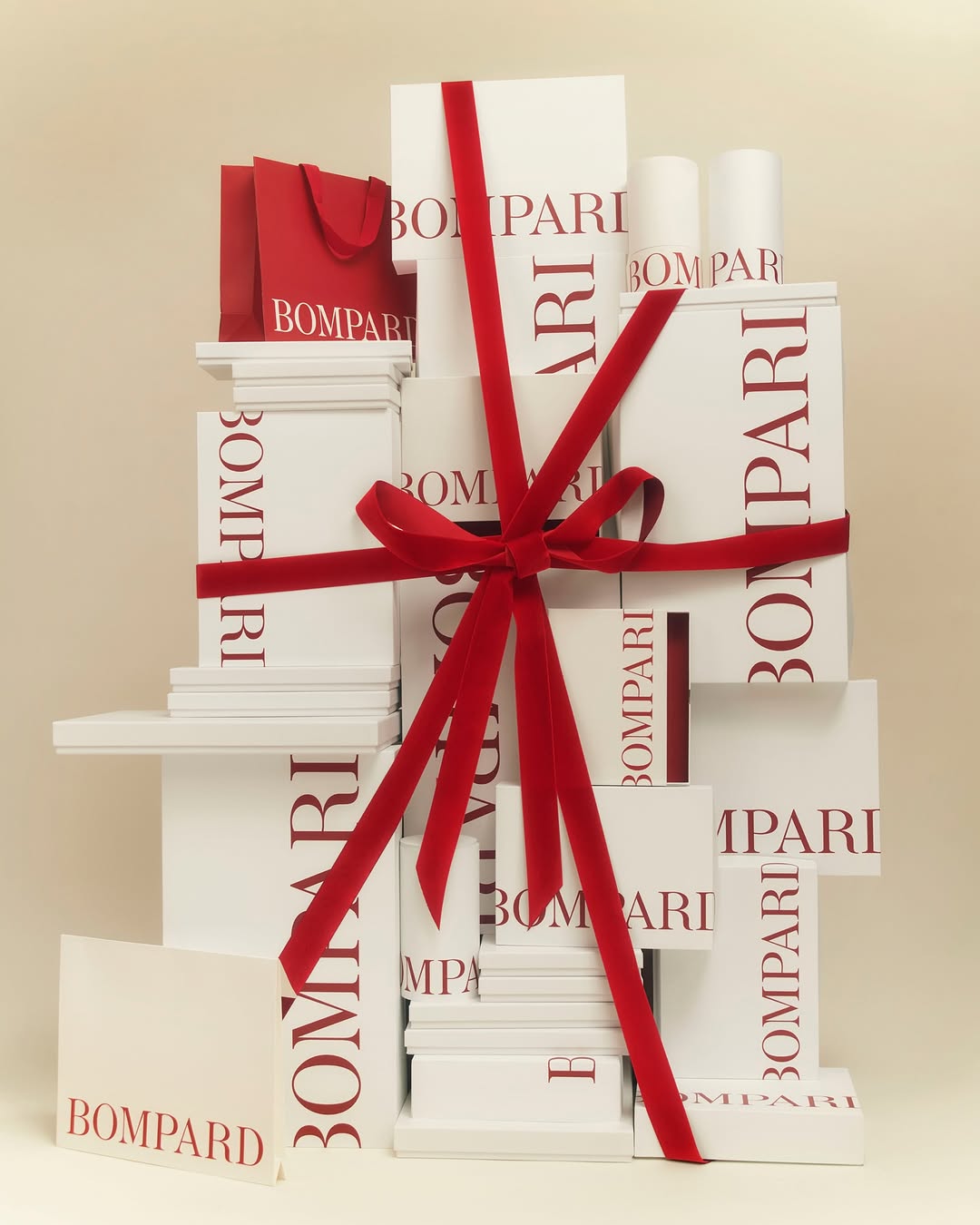 Stacked white Bomparti gift boxes tied with red velvet ribbon, accompanied by a red gift bag, creating a luxurious present display.