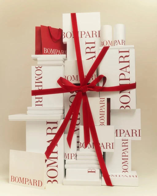 Stacked white Bomparti gift boxes tied with red velvet ribbon, accompanied by a red gift bag, creating a luxurious present display.