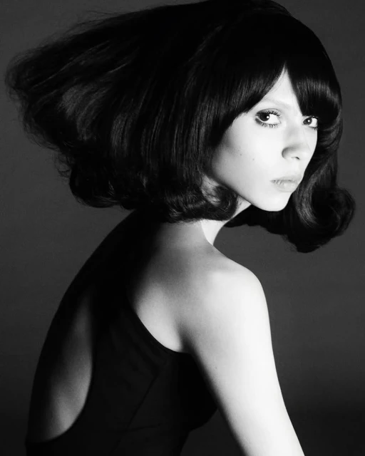Black and white portrait of a stylish woman with a dark bob hairstyle and retro fashion, captured in a studio setting with classic lighting.