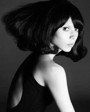 Black and white portrait of a stylish woman with a dark bob hairstyle and retro fashion, captured in a studio setting with classic lighting.