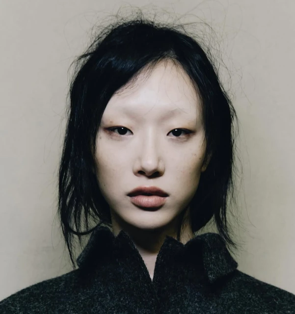 Close-up portrait of an Asian female model with dark hair and light skin wearing a gray wool coat against a neutral background.