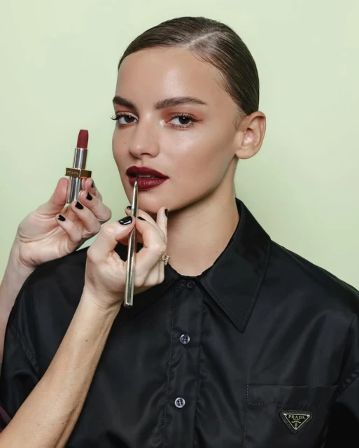 Close-up of a woman having dark red lipstick applied with a brush in a beauty studio setting, showcasing makeup artistry and products.