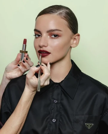 Close-up of a woman having dark red lipstick applied with a brush in a beauty studio setting, showcasing makeup artistry and products.