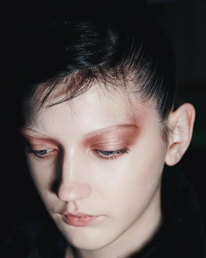 Close-up portrait of a woman with dramatic terracotta eyeshadow and slicked-back dark hair against a dark background