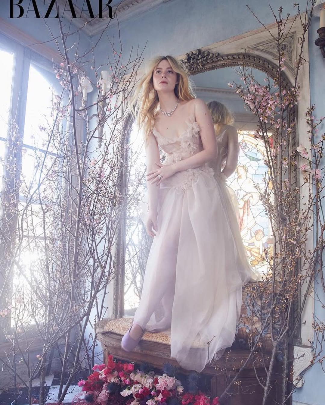 Elle Fanning in a light pink gown posing near a vintage mirror and dried flowers in a fashion editorial for Bazaar Magazine.