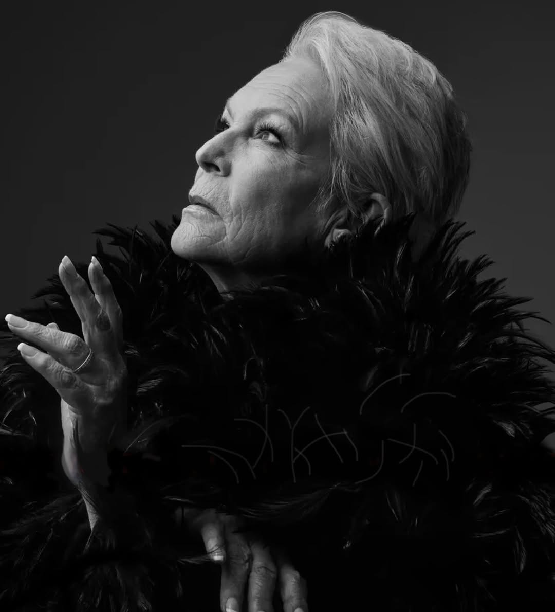 Elegant black-and-white portrait of an elderly woman with short white hair, adorned with a black feathered boa, looking upwards thoughtfully.