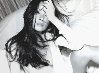 Black and white portrait of a woman with long dark hair running her hand through her hair, wearing a white top.