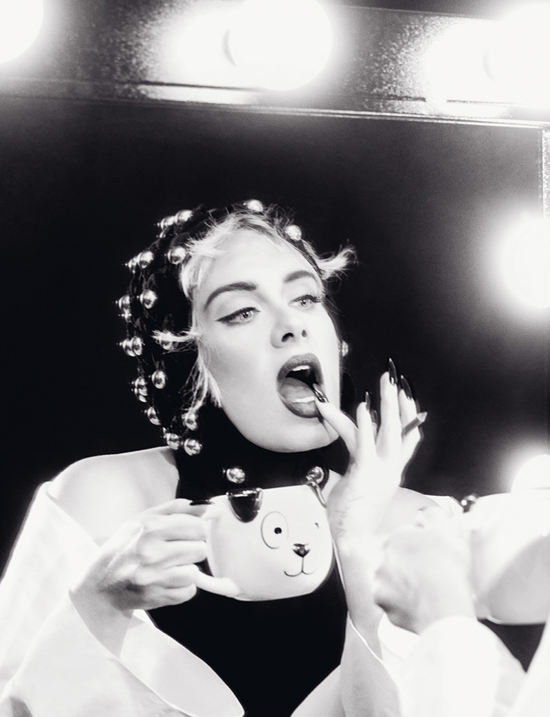 Black and white portrait of a fair-skinned adult female applying lipstick while holding a dog-themed mug and looking in a mirror.