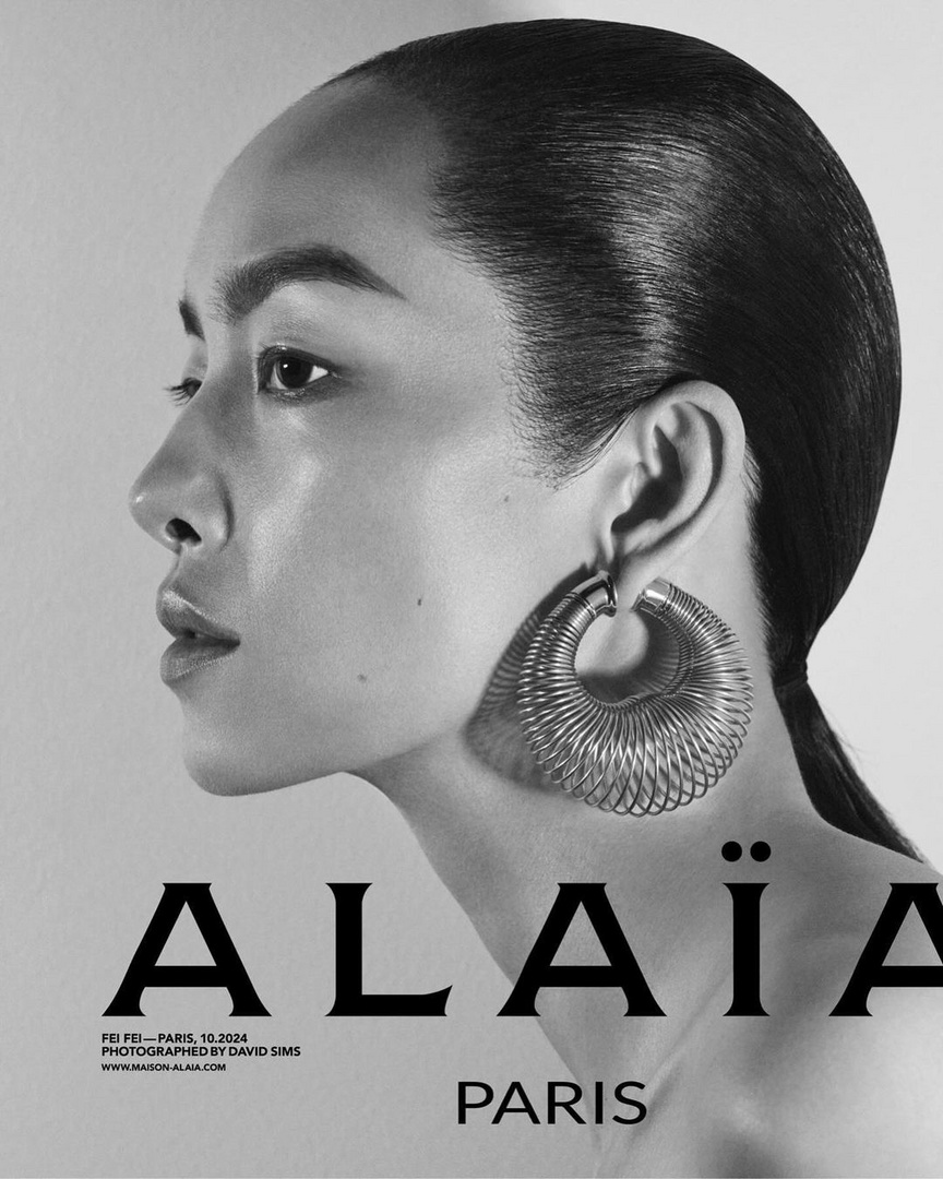 Monochrome headshot of a woman in profile with a sleek hairstyle and large hoop earring, against a grey background with brand typography.