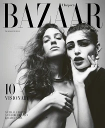 Two female models posing for a magazine cover with dark dramatic eye makeup and tousled hair against a plain grey studio background.