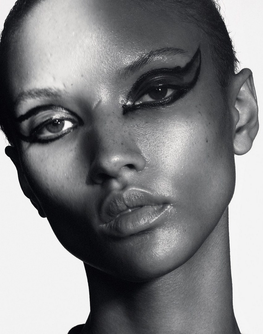 Close-up black and white portrait of a young woman with dramatic black graphic eyeliner against a stark white background in a beauty editorial.
