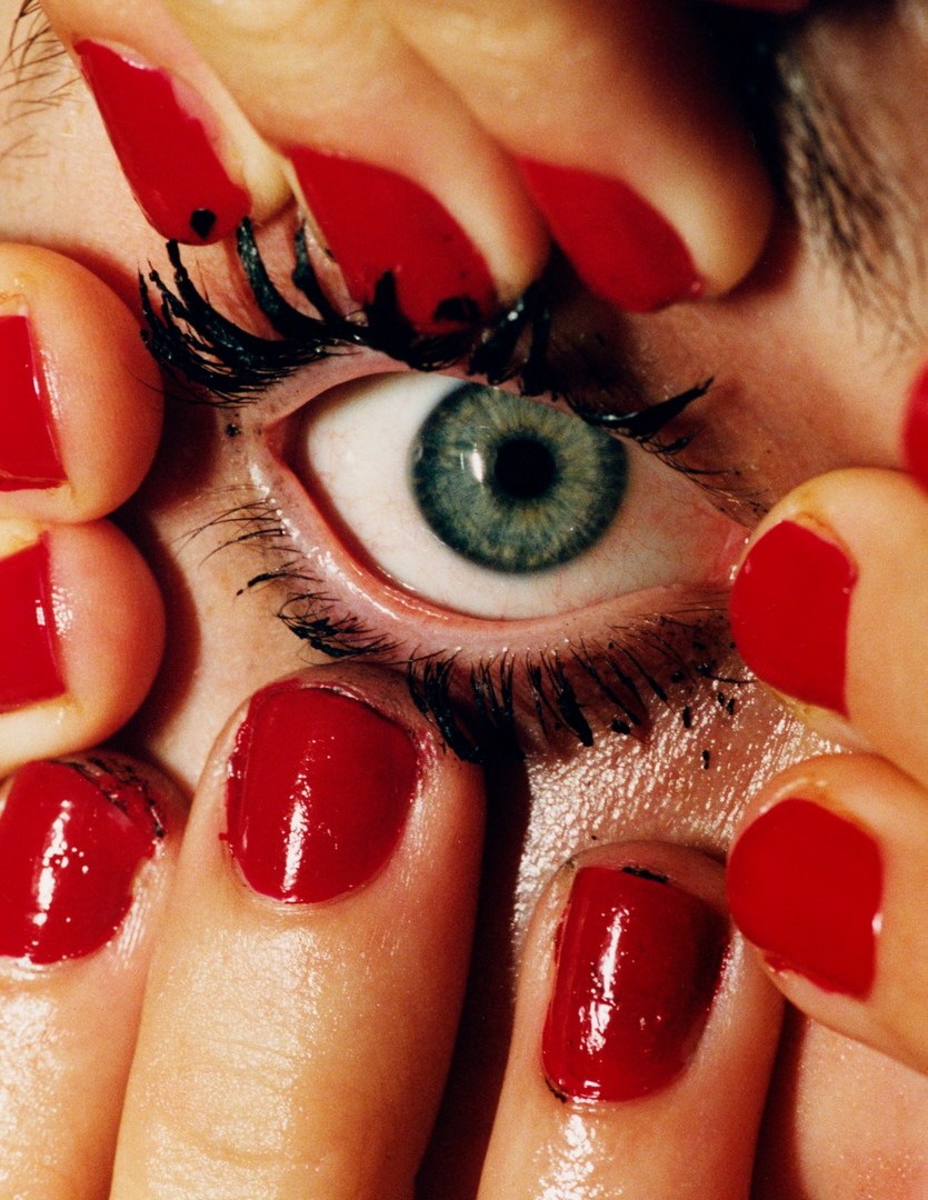 Close-up studio shot of a single eye surrounded by fingers with bright red nail polish, creating a visually striking beauty image.