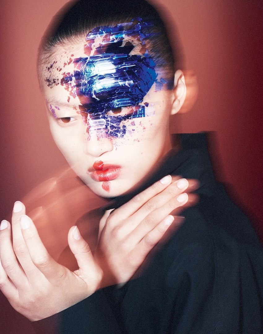 Model showcases artistic blue makeup with blurry hands in a studio setting, creating a striking beauty editorial shot.