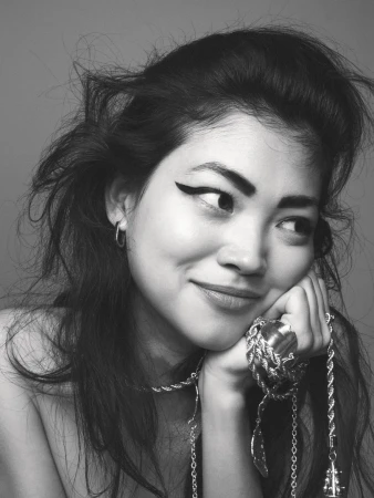 Close-up portrait of a woman with dramatic winged eyeliner resting her chin on her hand, wearing chunky silver jewelry.