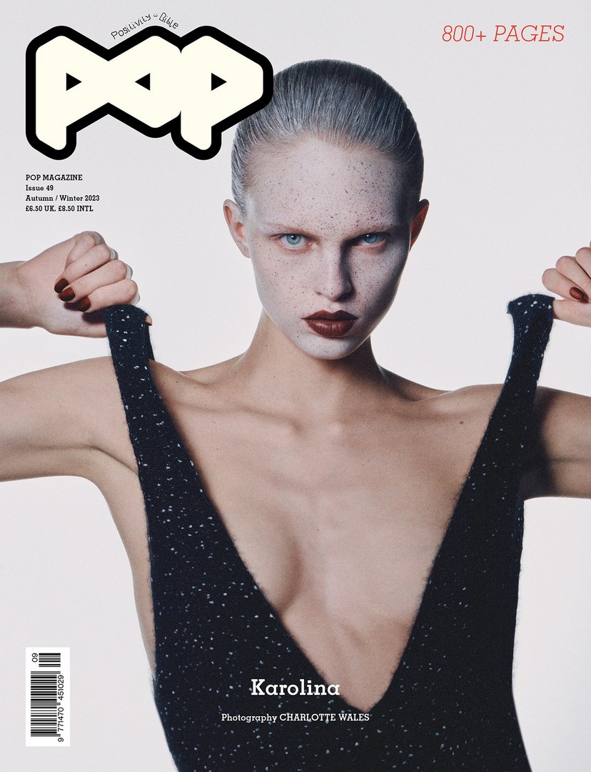 Pop Magazine cover featuring a model with pale skin and dark lipstick, holding the straps of a black, low-cut dress against a white background.