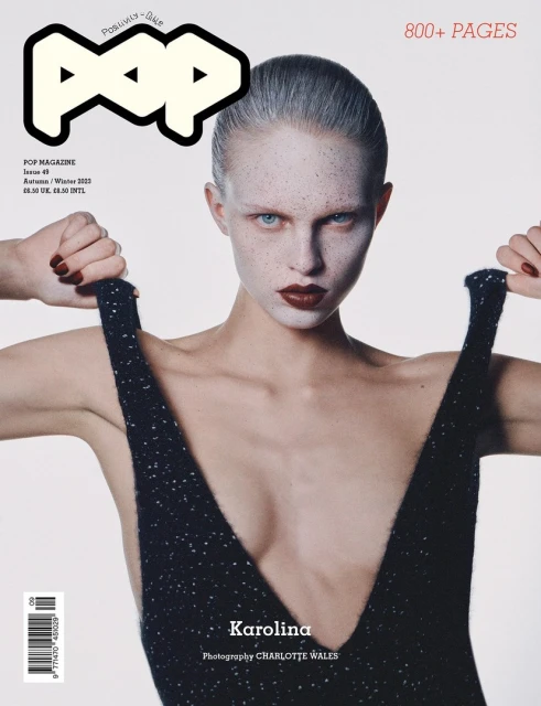 Pop Magazine cover featuring a model with pale skin and dark lipstick, holding the straps of a black, low-cut dress against a white background.