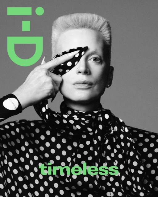 Magazine cover portrait of an adult with short blonde hair, wearing a black and white polka-dot top and holding polka-dot scarf.