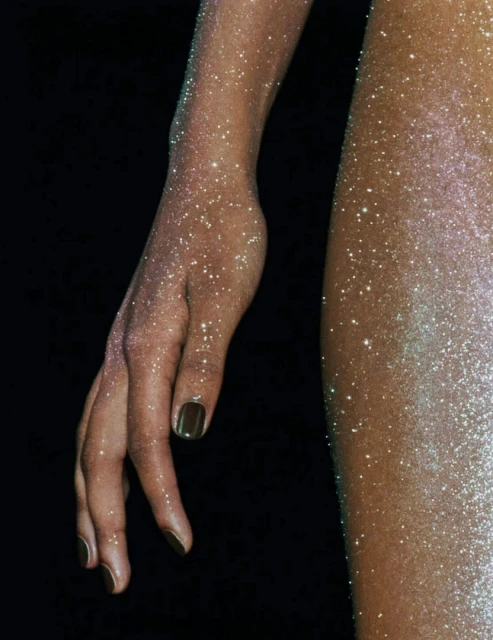 Close-up shot of an adult's arm and upper leg with glittery skin on a black backdrop, showcasing body art and creative cosmetic use.