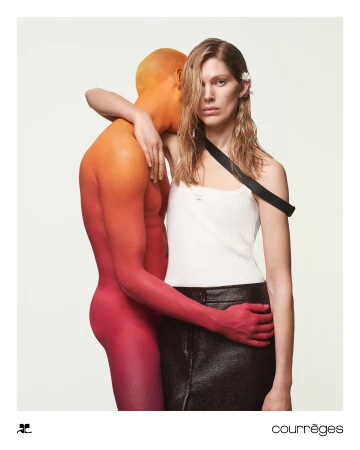 Woman in white tank top and dark skirt standing beside a body-painted figure with gradient orange and red skin.