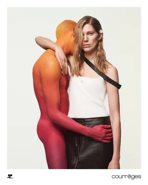 Woman in white tank top and dark skirt standing beside a body-painted figure with gradient orange and red skin.