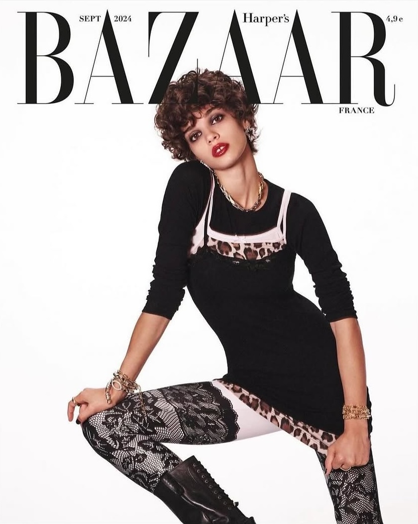 Bazaar France cover featuring a woman with curly hair in a black long-sleeved dress, lace leggings, and black boots, with a white background.
