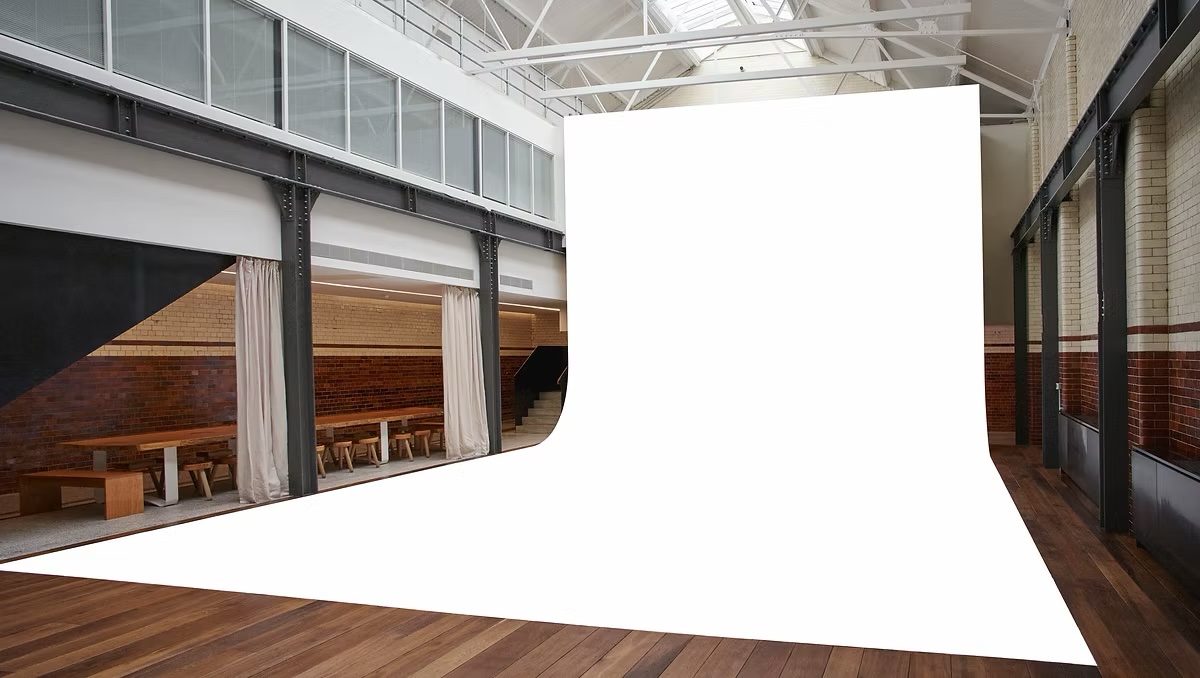 Blank white backdrop fills a modern interior space with wooden floors, brick walls, high ceilings, and natural light from windows.