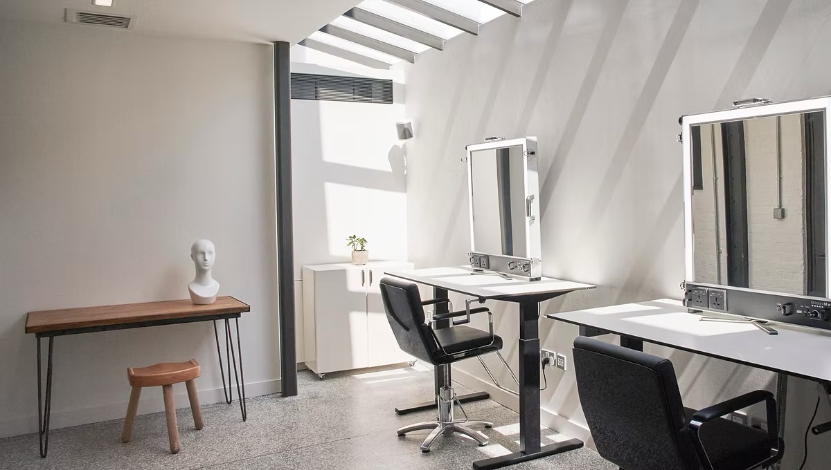 Bright and airy interior of a hair salon with mirrors, styling stations, chairs, and a mannequin head, illuminated by natural light.