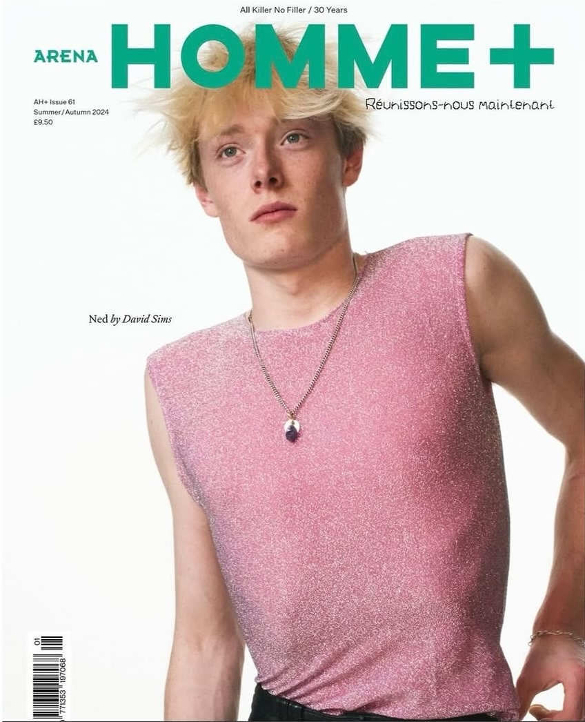 Magazine cover featuring a blond male model in a pink top and black pants with a white background, showcasing fashion and style.
