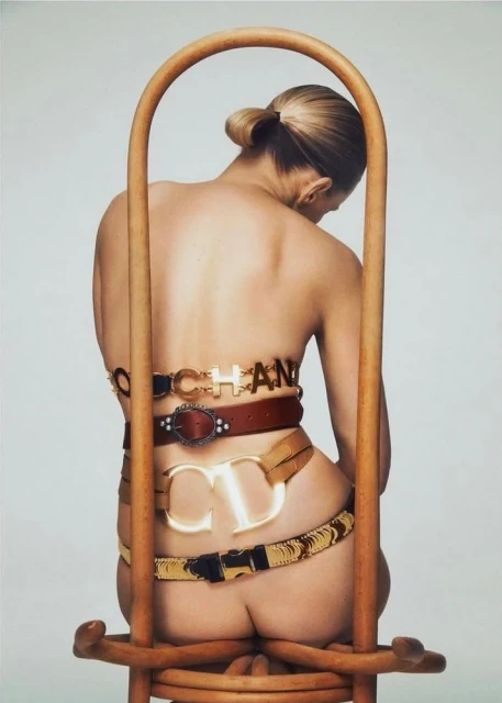 Model seated facing away from camera wearing multiple belts around waist against a light background