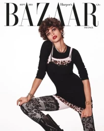 Model with short curly brown hair wearing a black top and lace patterned leggings against a white background