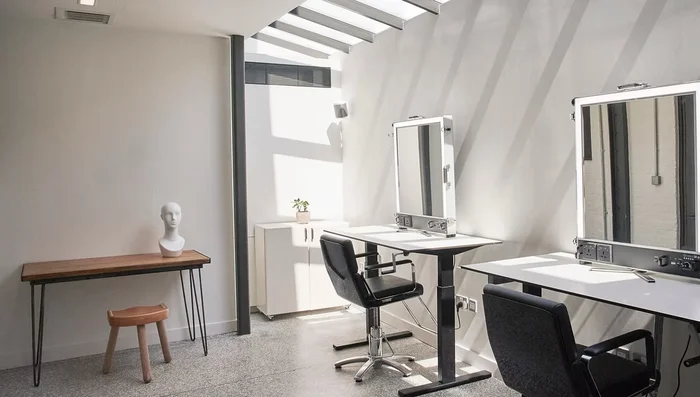 Bright photo studio interior in London with vanity mirrors, styling desks, and modern black chairs.