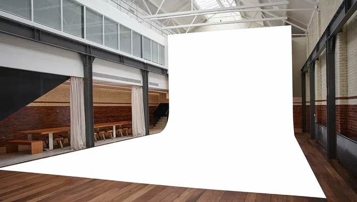 Spacious photo studio in London with large white sweep, hardwood floors, exposed brick walls, and steel support beams.