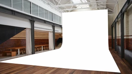 Spacious photo studio in London with large white sweep, hardwood floors, exposed brick walls, and steel support beams.
