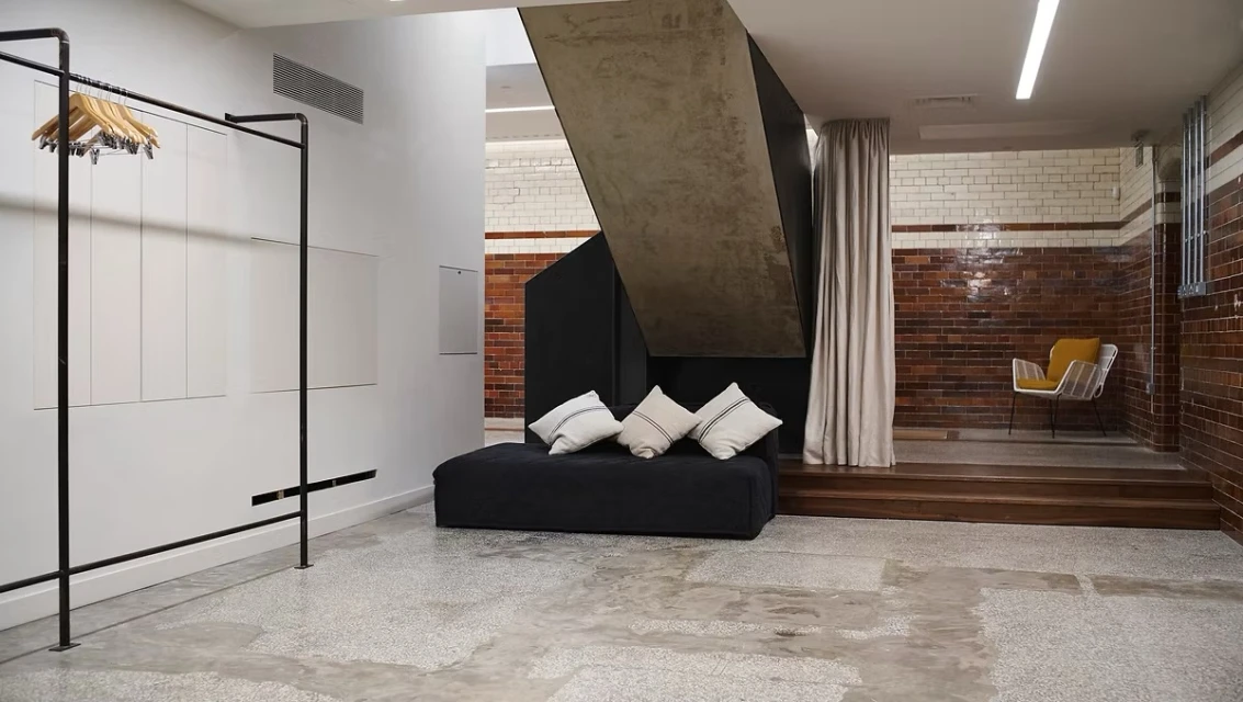 Modern interior space with white walls, brown tiled lower walls, black daybed with pillows, and a metal clothing rack.