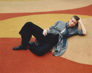 Person reclining on a textured multi-colored rubber playground surface wearing a grey belted coat and black trousers
