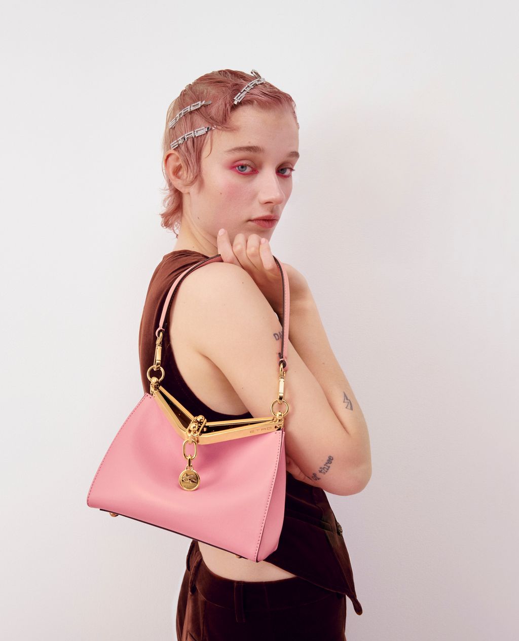 Close-up of a young fair-skinned adult female wearing a brown top and pink purse with a white studio background.