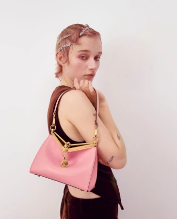 Close-up of a young fair-skinned adult female wearing a brown top and pink purse with a white studio background.