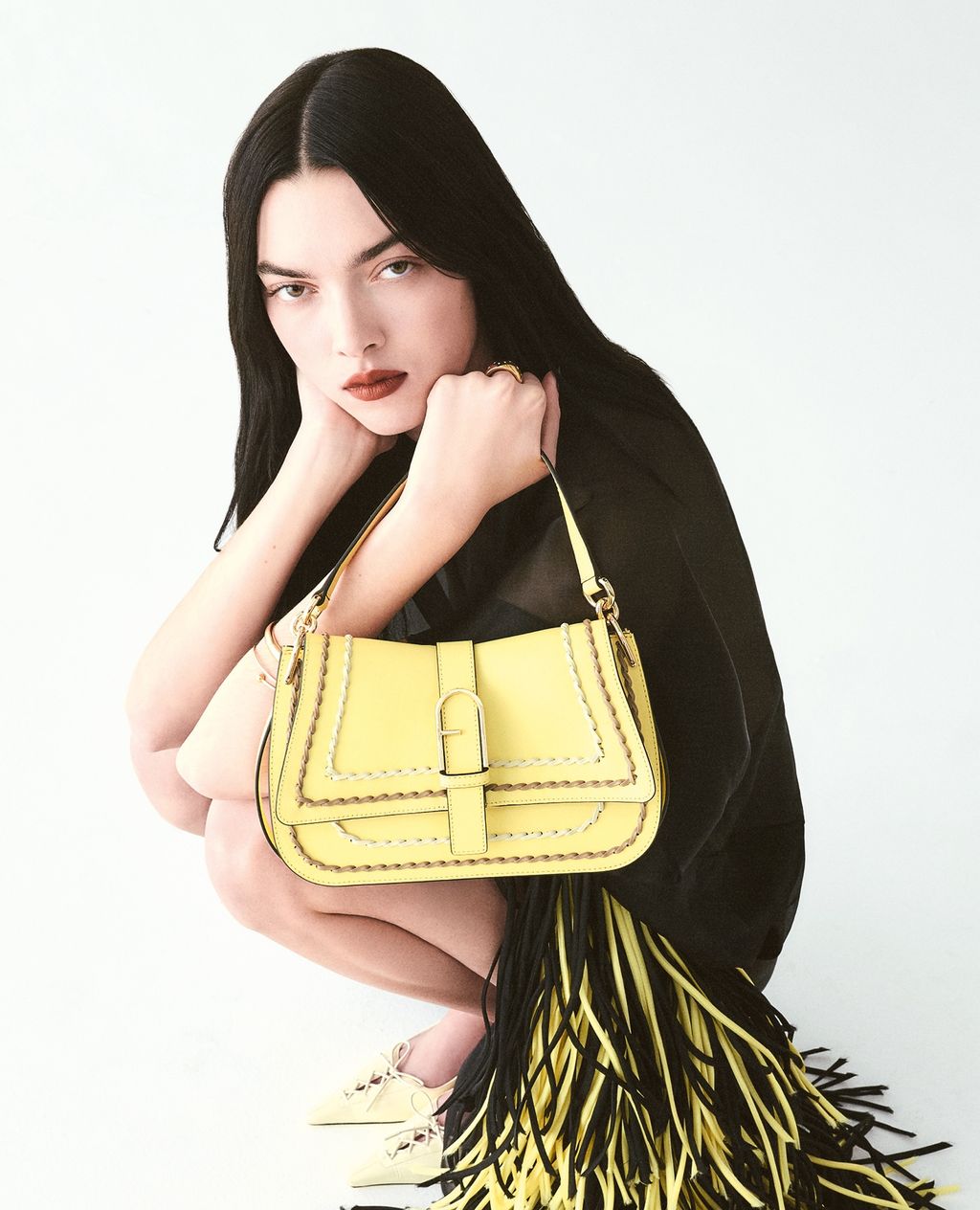 Woman poses in a studio with a yellow leather purse featuring whipstitch details and fringe against a white backdrop.