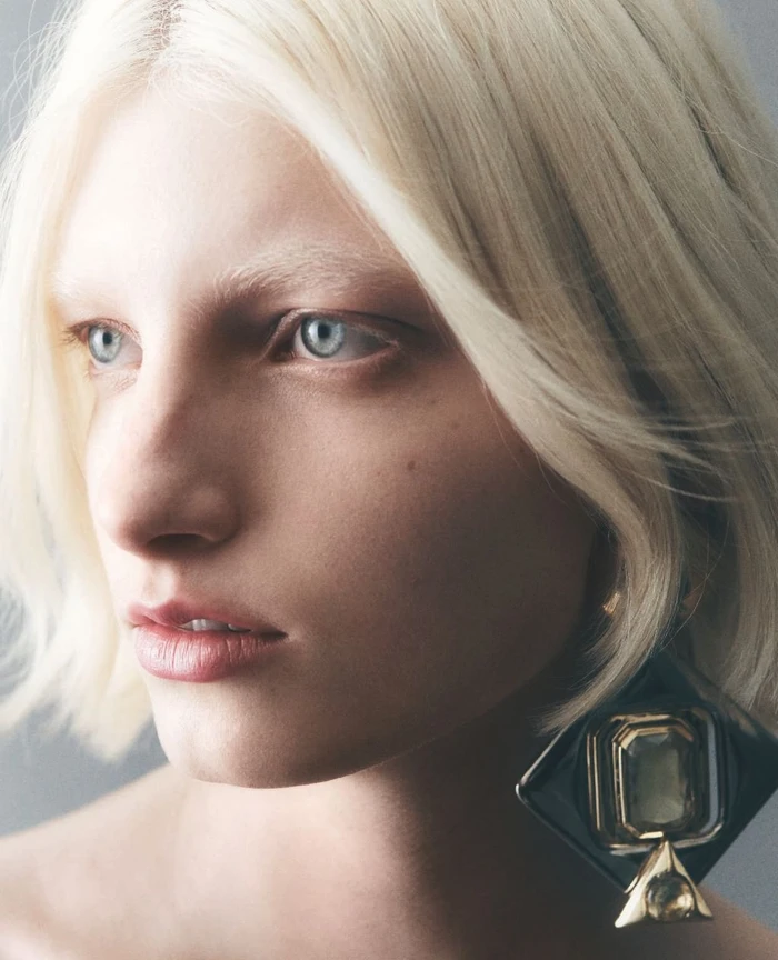 Close-up portrait of a blonde woman wearing large statement earrings with makeup by Tanja Friscic in Milan