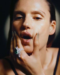 Close-up portrait of a woman touching her face with long manicured nails and a large statement ring, by make-up artist Tanja Friscic.