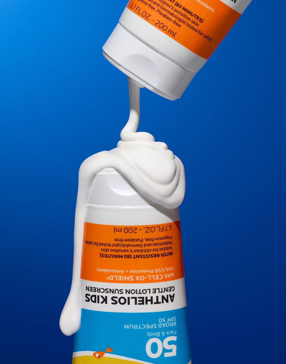 Two tubes of sunscreen, one upside down, dispensing cream onto the other against a blue background, creating a visually appealing product shot.