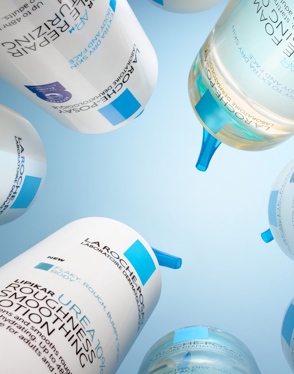 Several white and blue La Roche-Posay skincare product bottles and jars are arranged against a gradient blue background in a beauty product shot.