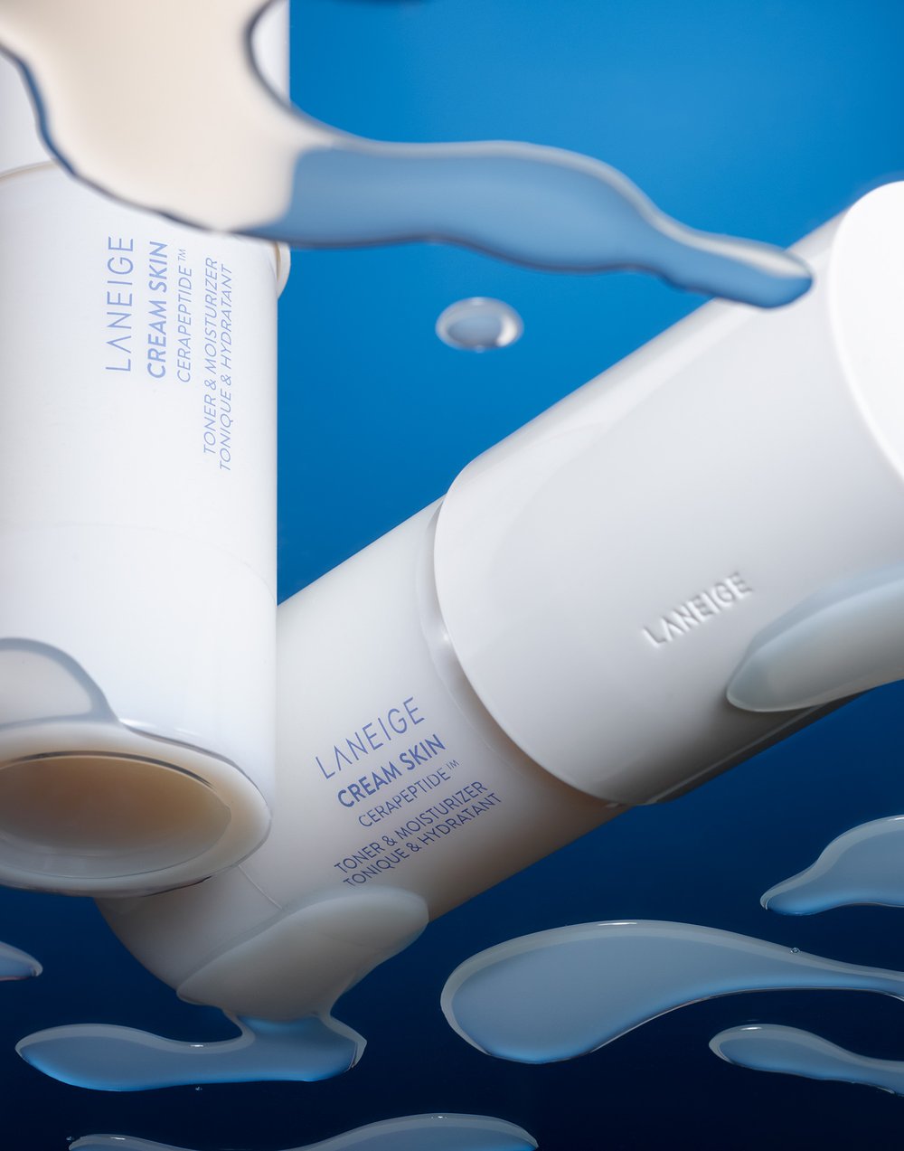 Close-up of three white Laneige Cream Skin toner bottles with blue liquid accents against a graduated blue background in studio light.