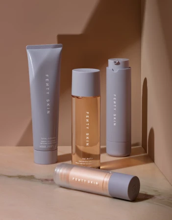 Four Fenty Skin skincare products arranged upright and lying down on a warm beige marble surface in front of a matching backdrop.